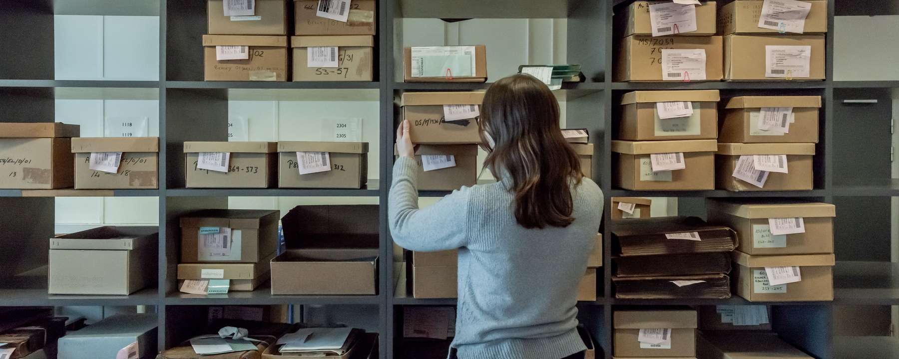 A person stands in front of an archive shelf full of boxes.