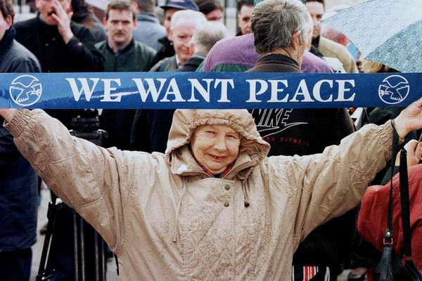 A smiling woman holds up a banner reading 'We want peace'.