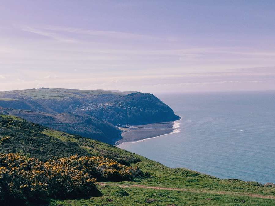 A colourful photograph showing the sea and green landscape.