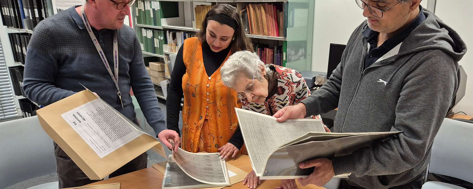 Four people of different ages are engrossed reading copies of historical documents around a table.