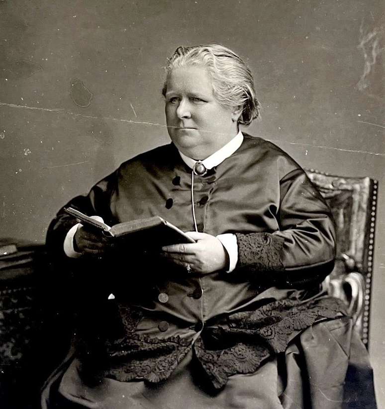 A photograph of Miss Frances Power Cobbe. She is seated, wearing black with a white collar, and holding an open book..