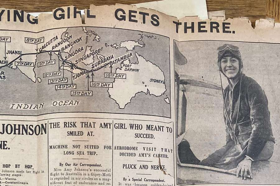 An old newspaper with tattered edges showing a photo of Amy Johnson smiling at the camera and a map of her route from Britain to Australia.