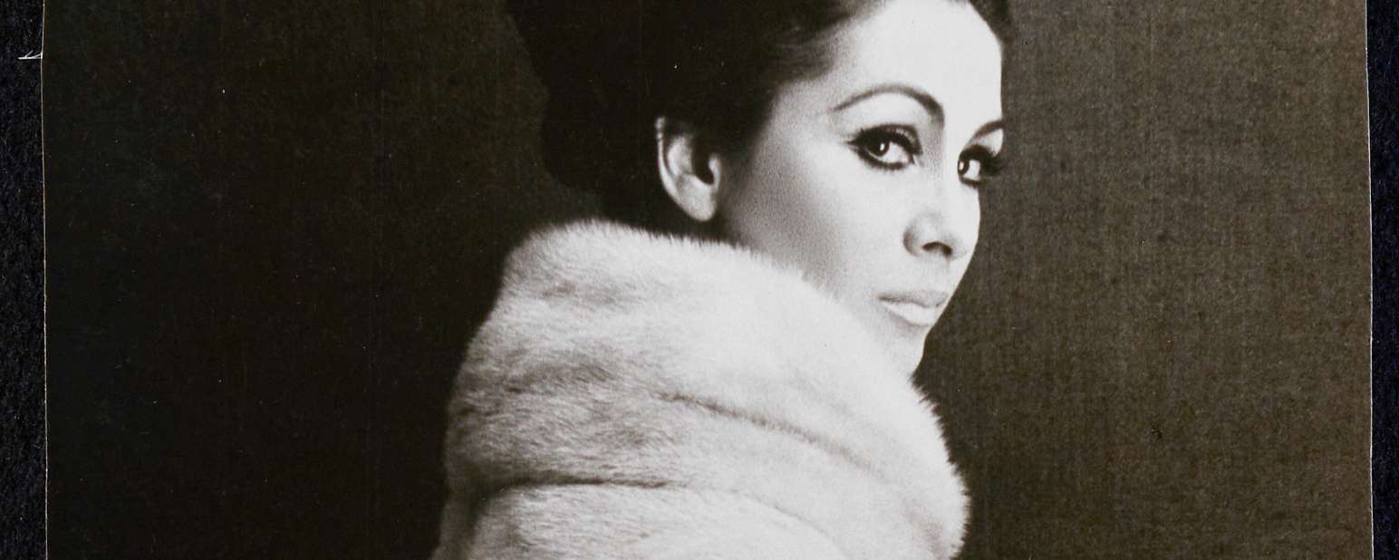 A black and white photo of a woman in a fur coat looking over her shoulder at the viewer.