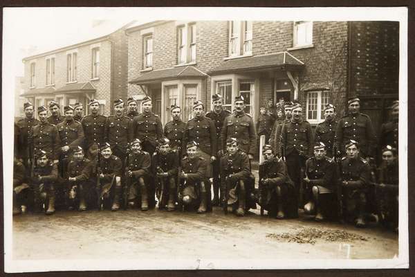 Photograph of a group of First World War soldiers posing in front of a row of houses.