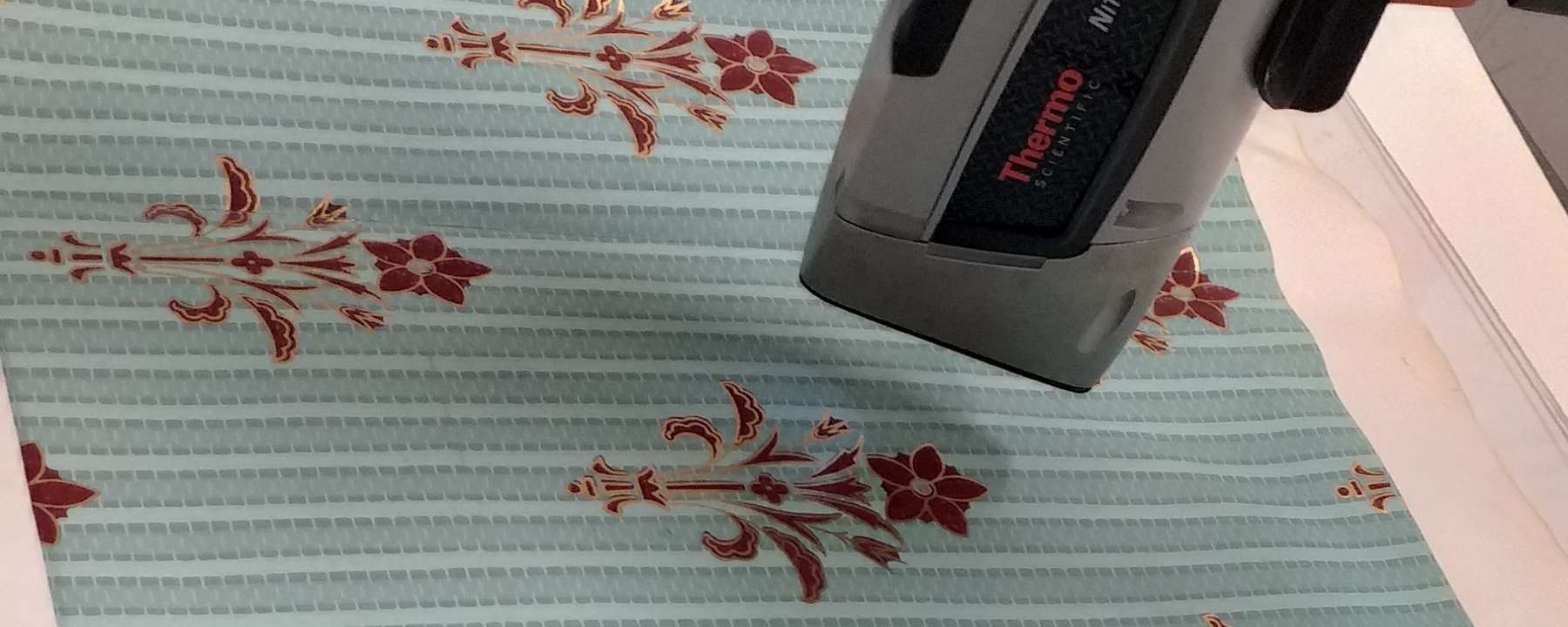 A scientific instrument analyses a blue textile with red flowers