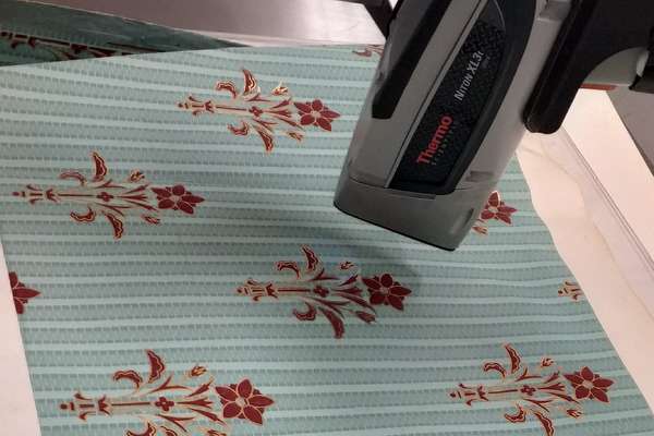 A scientific instrument analyses a blue textile with red flowers
