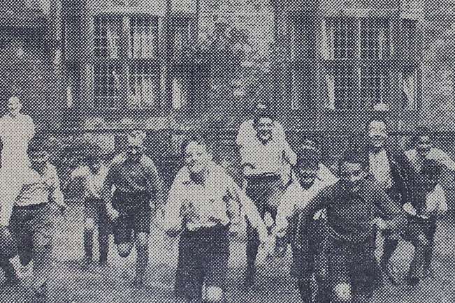 Grainy newsprint photograph of a group of children running towards the camera. They are smiling and laughing.