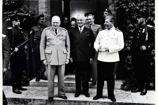 Winston Churchill, Harry Truman and Joseph Stalin stand smiling next to each other, with soldiers on either side.