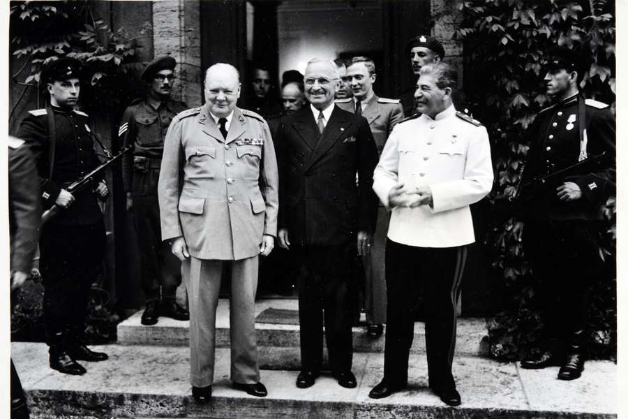 Winston Churchill, Harry Truman and Joseph Stalin stand smiling next to each other, with soldiers on either side.