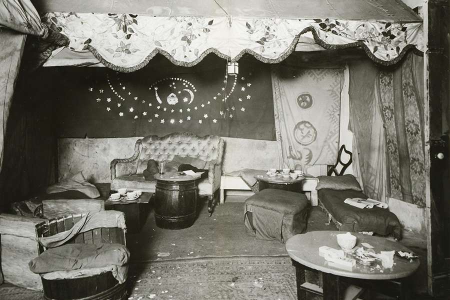The interior of a club with no people. It is full of soft furnishings, tables and draped fabric