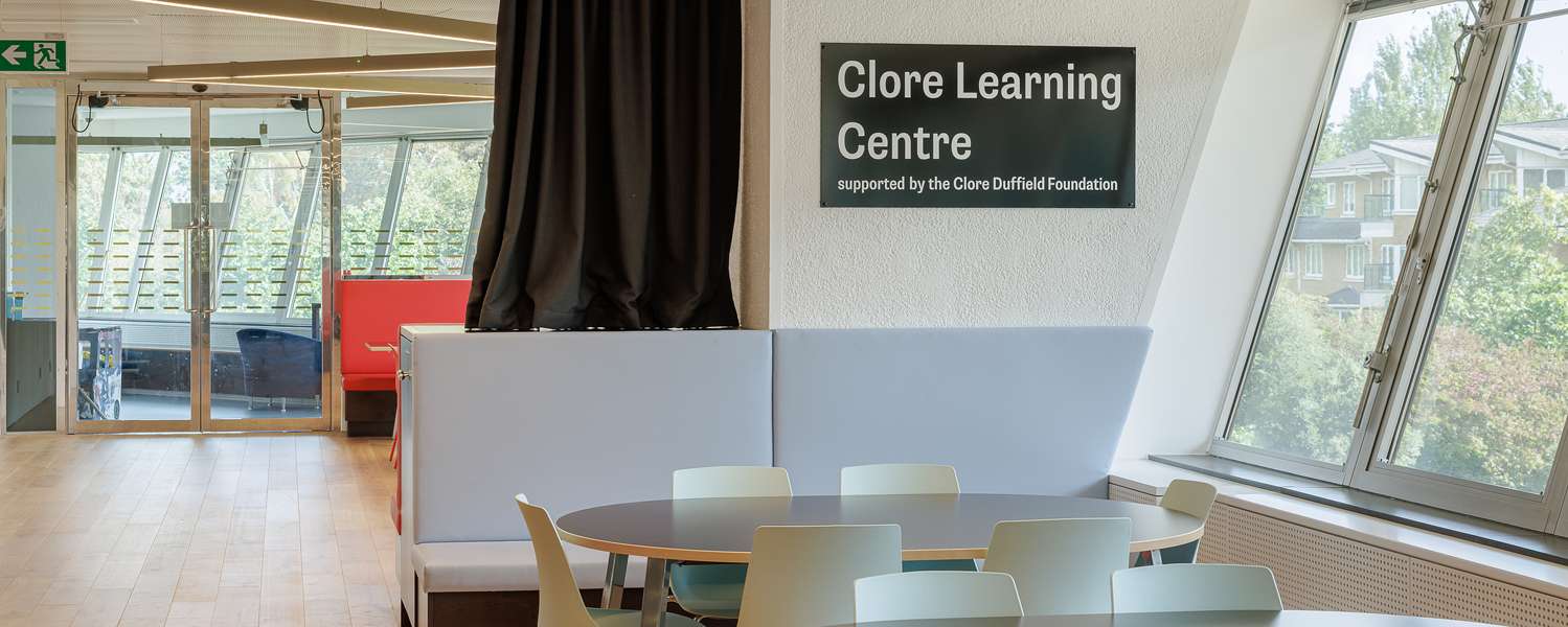 A bright and airy room with soft seating and tables with chairs. A sign on the wall reads 'Clore Learning Centre'.