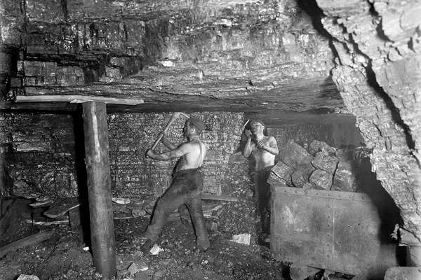 Photograph of two coal miners working underground with pick axes.
