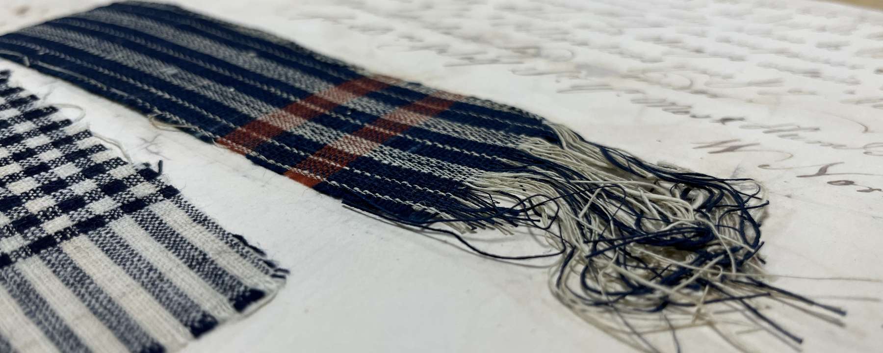 Two samples of checked cotton material in blues, whites, reds, and blacks, found within the collections related to the PASSAGE project.