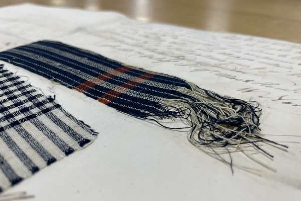 Two samples of checked cotton material in blues, whites, reds, and blacks, found within the collections related to the PASSAGE project.