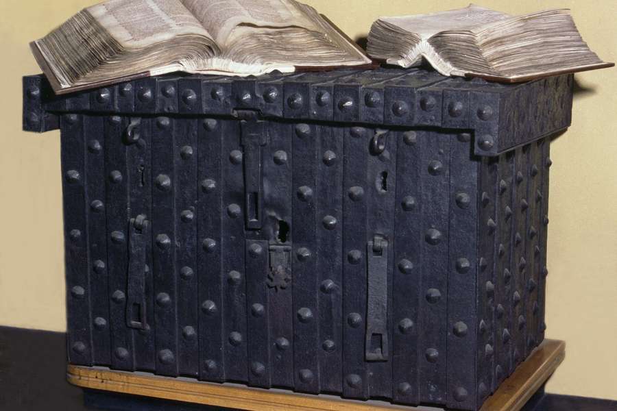 A large and secure old chest with two old books open on top of it.