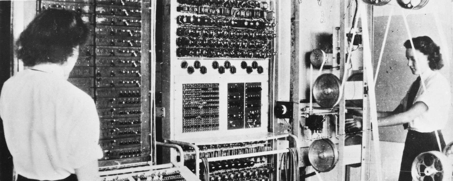 Black and white photograph of two women standing in front of the Colossus electronic digital computer.