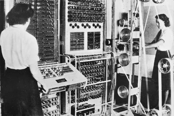 Black and white photograph of two women standing in front of the Colossus electronic digital computer.