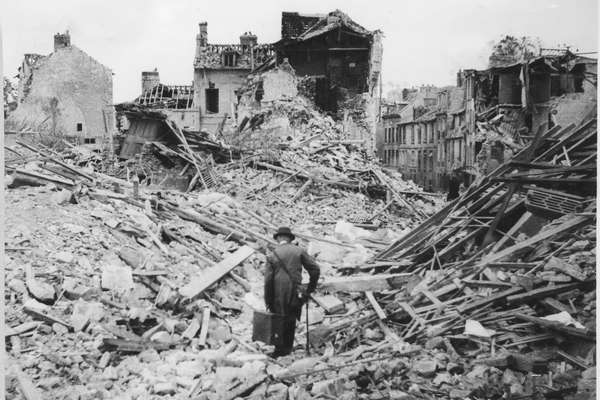 Black and white photo of bomb damage, a man with a walking stick is walking towards bombed rubble