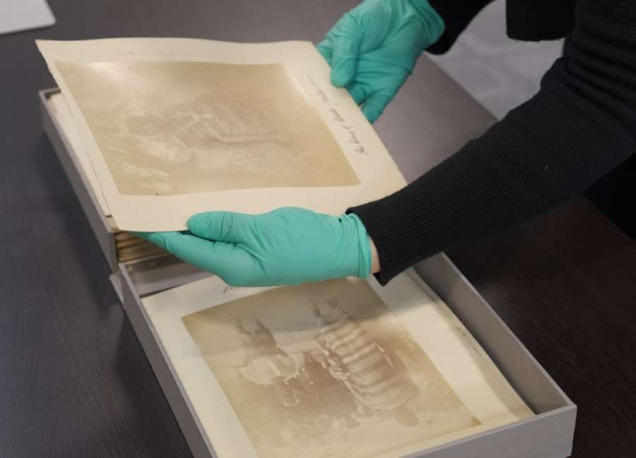 Hands in teal nitrile gloves handing two photographs of people on top of a paper page.