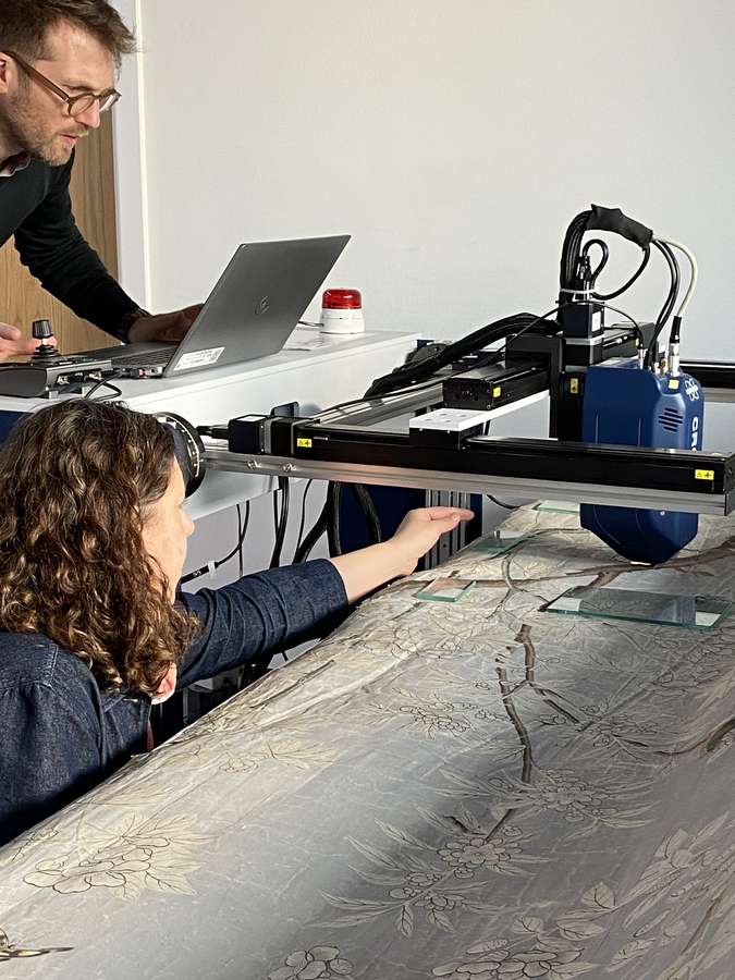 Two researchers use x-ray fluorescence equipment to examine grey Chinese wallpaper