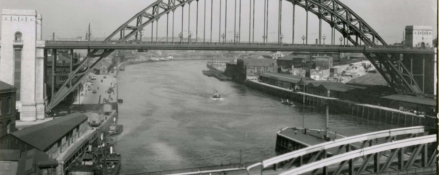 Photograph of the Tyne Bridge, a large through arch bridge positioned high over the river. A smaller bridge is visible in the foreground.