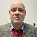 James is wearing a Christmas jumper under a beige checked blazer