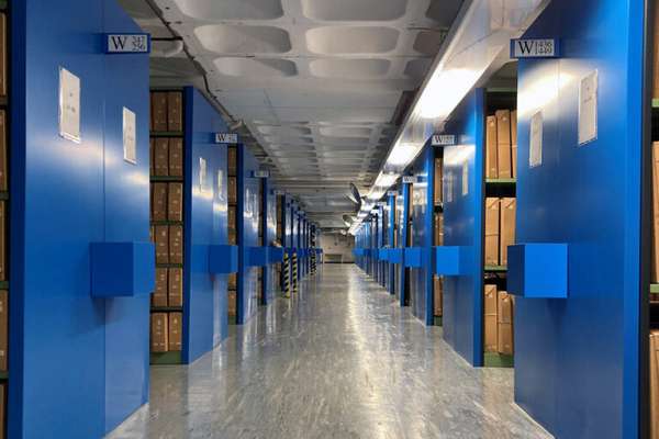 A vast windowless room filled with shelves. On the shelves are rows of archival boxes.