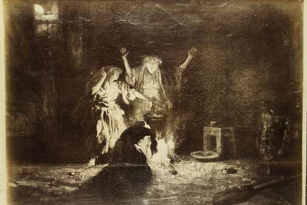 Black and white image showing two standing figures and one kneeling down stirring a fire with a pot above it.