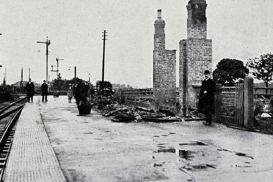 Photograph of a train station platform with a building that has been burned down.