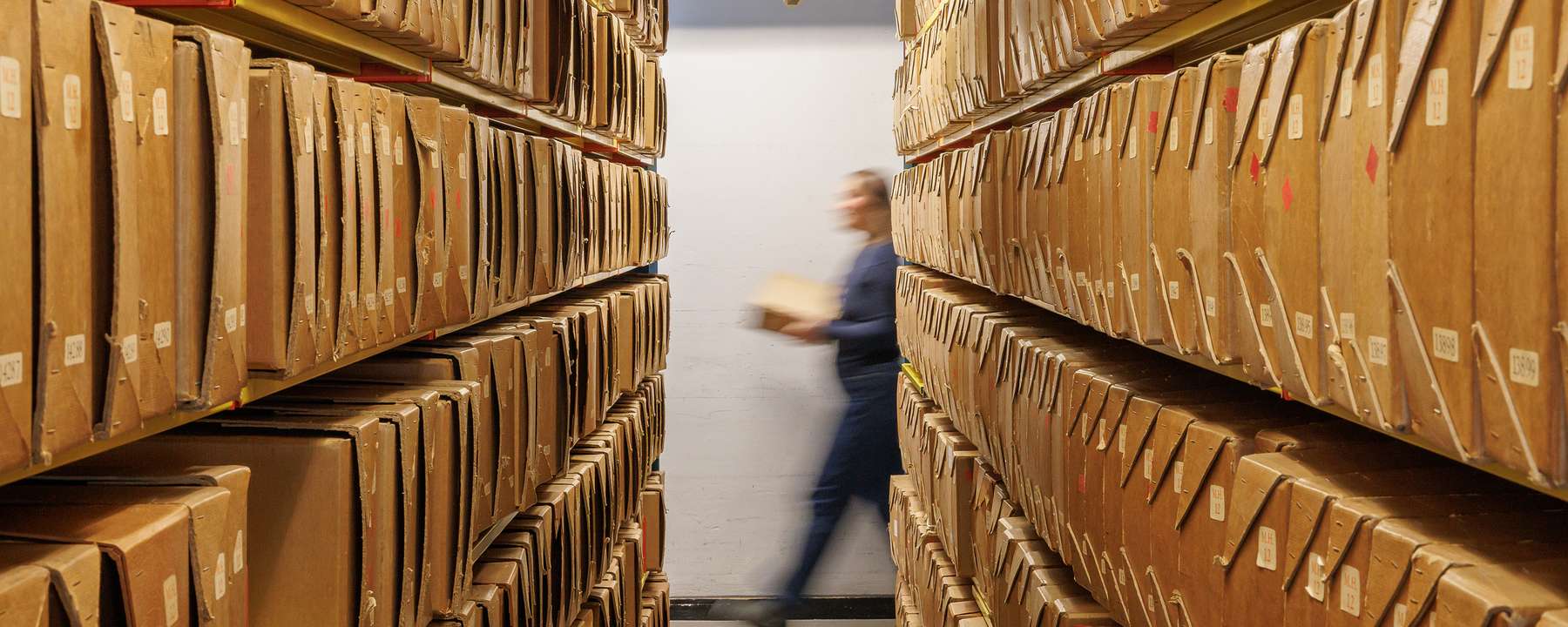 An archivist walks past shelves full of archival boxes.