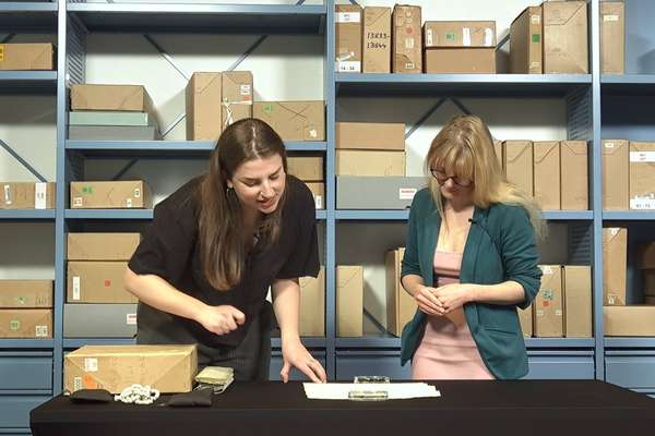 Two archive specialists stand over and discuss a record in a repository at The National Archives.
