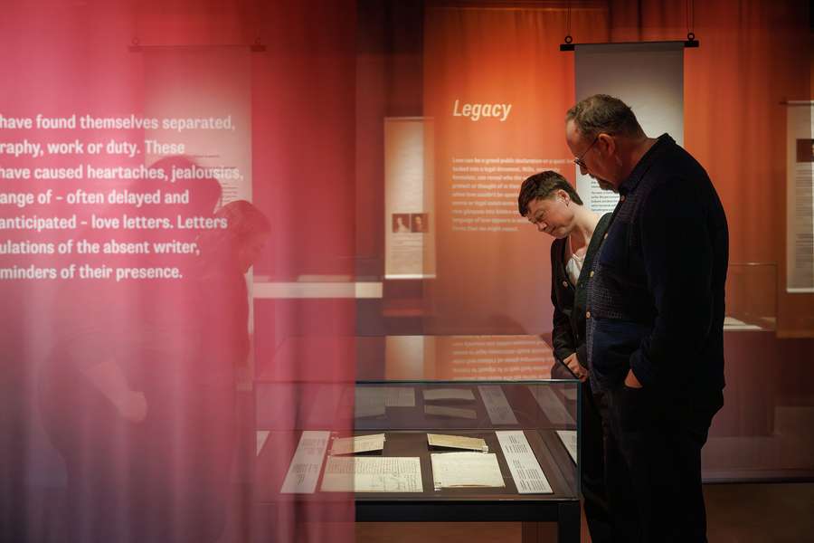 Inside an exhibition. Two visitors look at a case of documents.