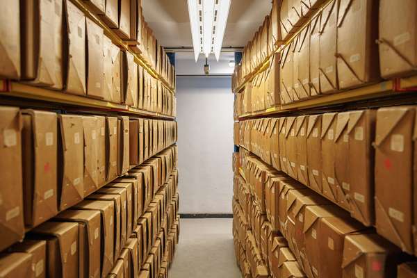 An aisle passes between boxes of archival records, tightly packed, seven shelves high.