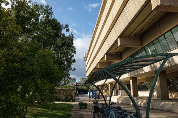 A covered bike shelter sits between The National Archives Building and a grassy bank.