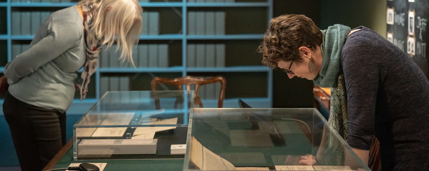 Two visitors looking down at documents in display cases in the MI5: Official Secrets Exhibition.