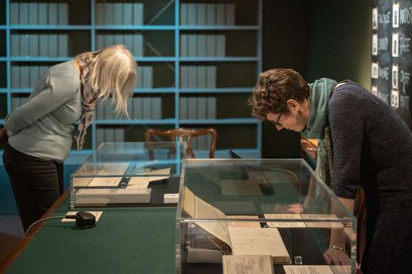 Two visitors looking down at documents in display cases in the MI5: Official Secrets Exhibition.