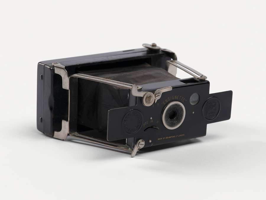 A small black camera made entirely of metal, with leather bellows extending to the lens.