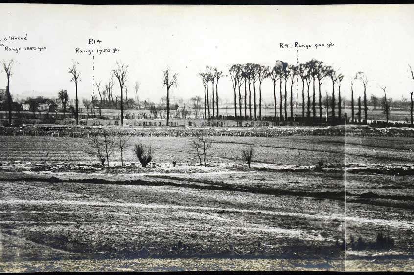 Landscape photo showing bare fields with trenches dug in, and a row of thin trees.