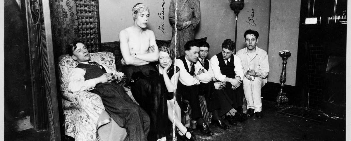 Eight people seated, one standing, in a room looking at the camera.