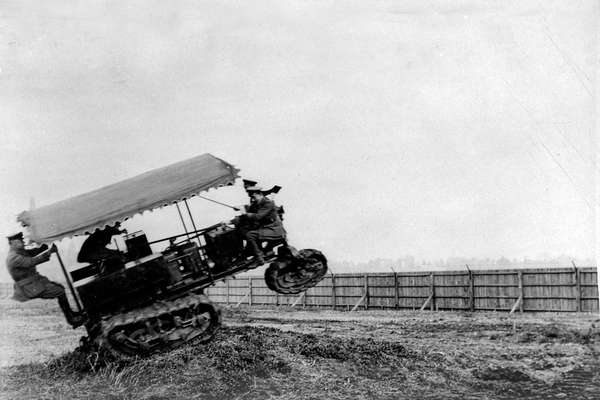 A photograph of an early tank moving a fast speed over a bump with people inside.