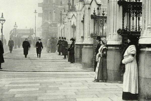 A photo of two women standing besides pillars outside the House of Commons. Police are watching on.