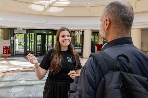 A visitor talks to a member of staff in The National Archives foyer, with rotating doors in the background.