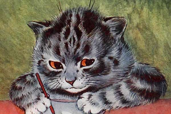A grey cat leans over a piece of paper and holds a pencil in its hand. It's drawing a rabbit