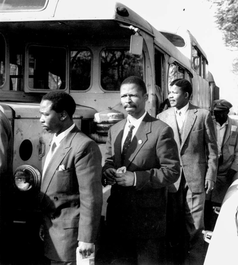 A line of men dressed smartly in suits and ties walk off a bus.