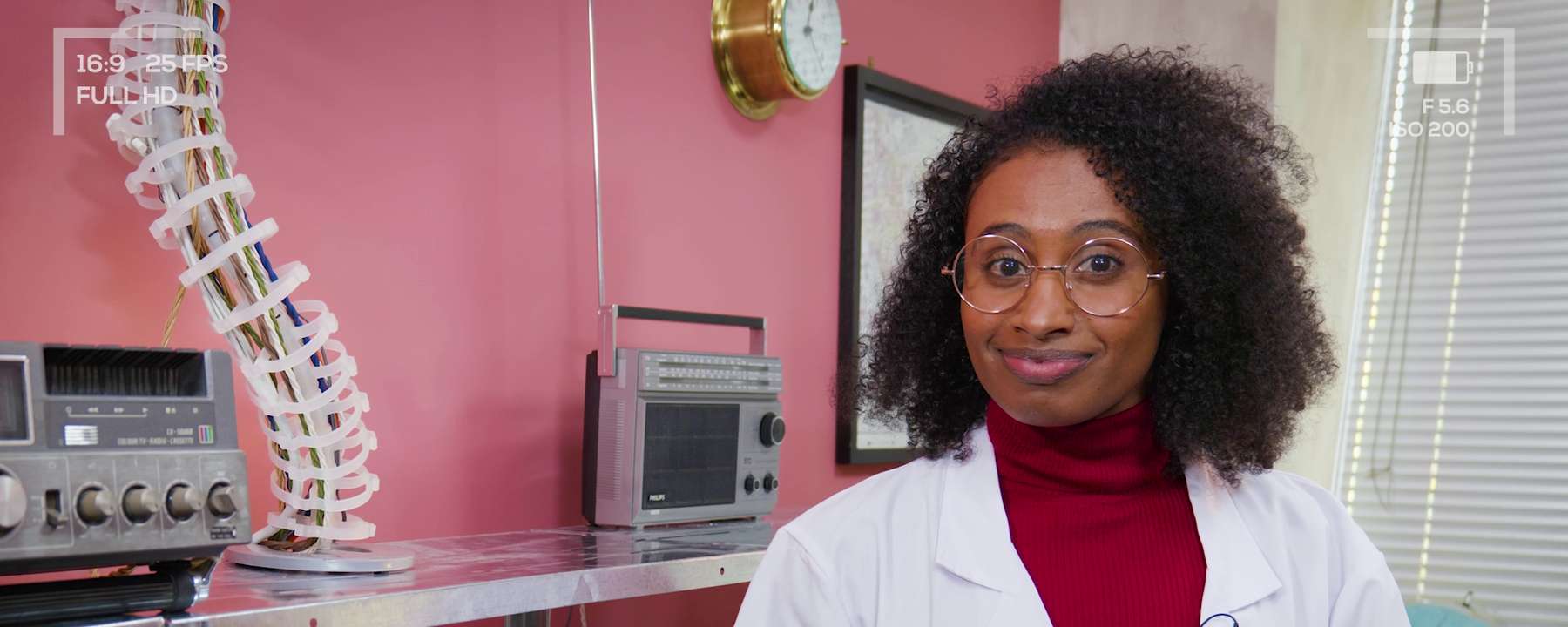 A smiling woman in a lab coat, surrounded by electronic equipment.