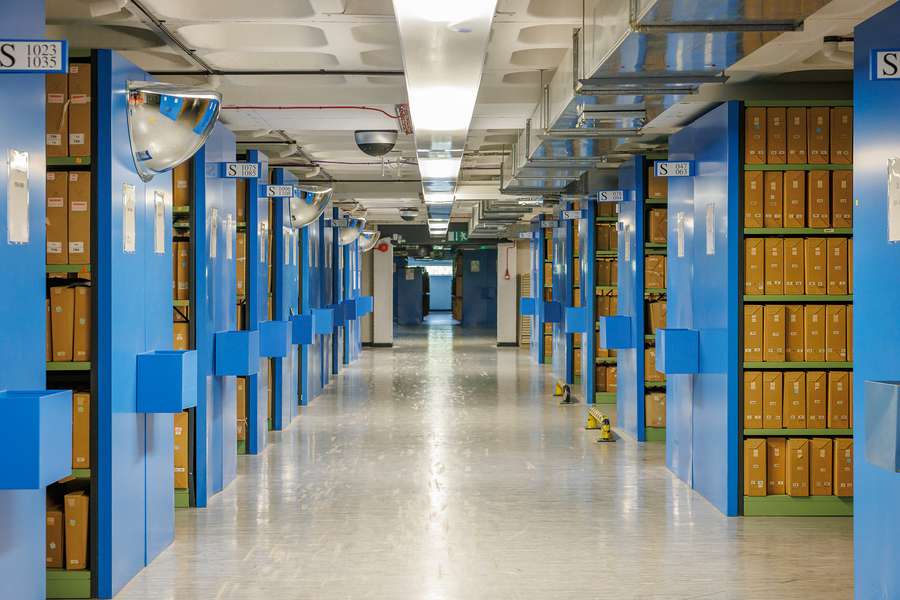 A vast windowless room filled with shelves. On the shelves are rows of archival boxes.