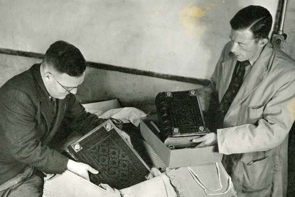A black and white photo of two men taking books from our collection out of a box