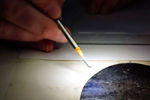 Close up of a hand holding a fine scalpel hovering over an old document.