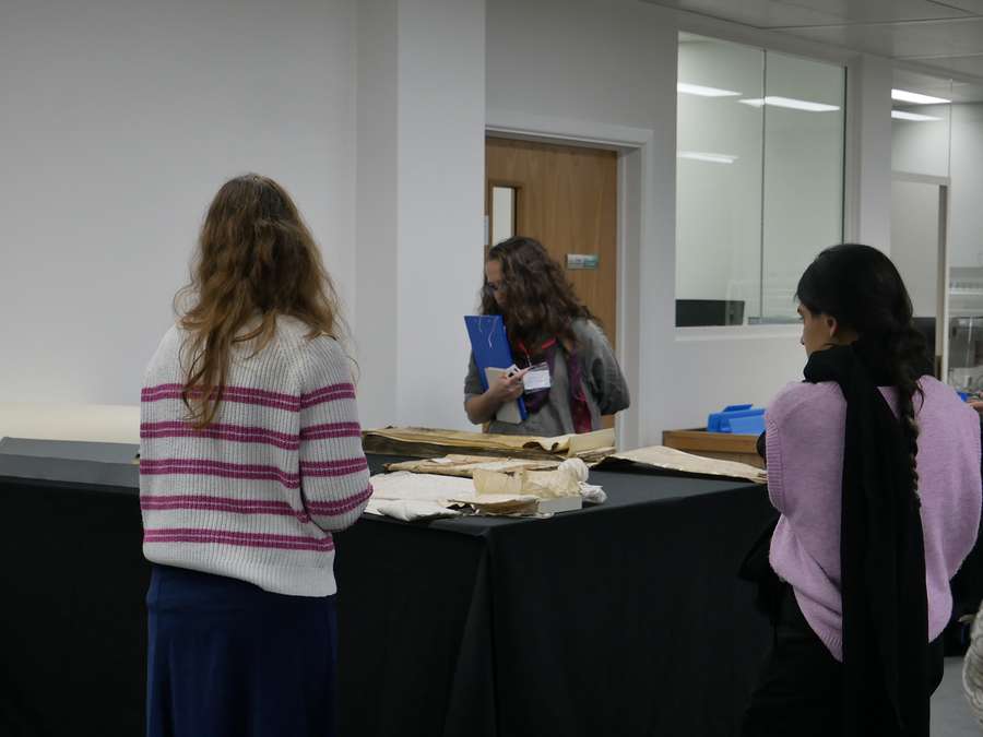 Three people standing in front of a table in the Collection Care Studio at The National Archives. They are looking at records that are placed on the table.