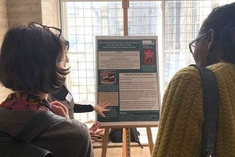 Three people read a poster filled with information that is standing on an easel.